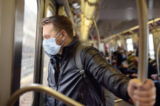 Mature man wearing disposable medical face mask in car of the subway in New York during coronavirus outbreak