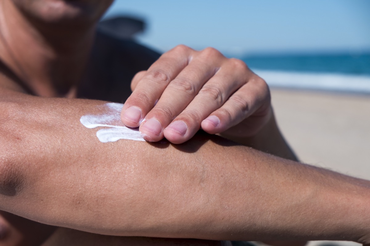 man on the beach man applying sunscreen to his arm