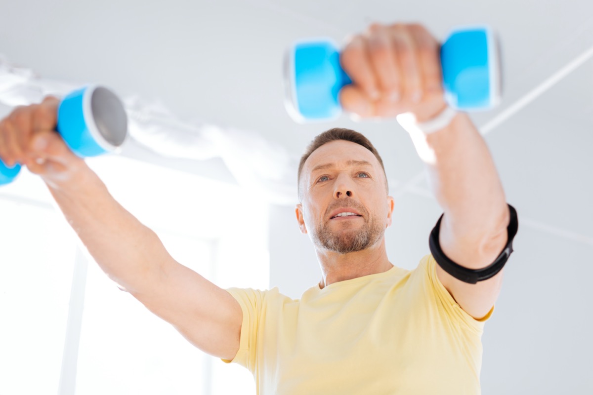 man smiling while using dumbbells and working out