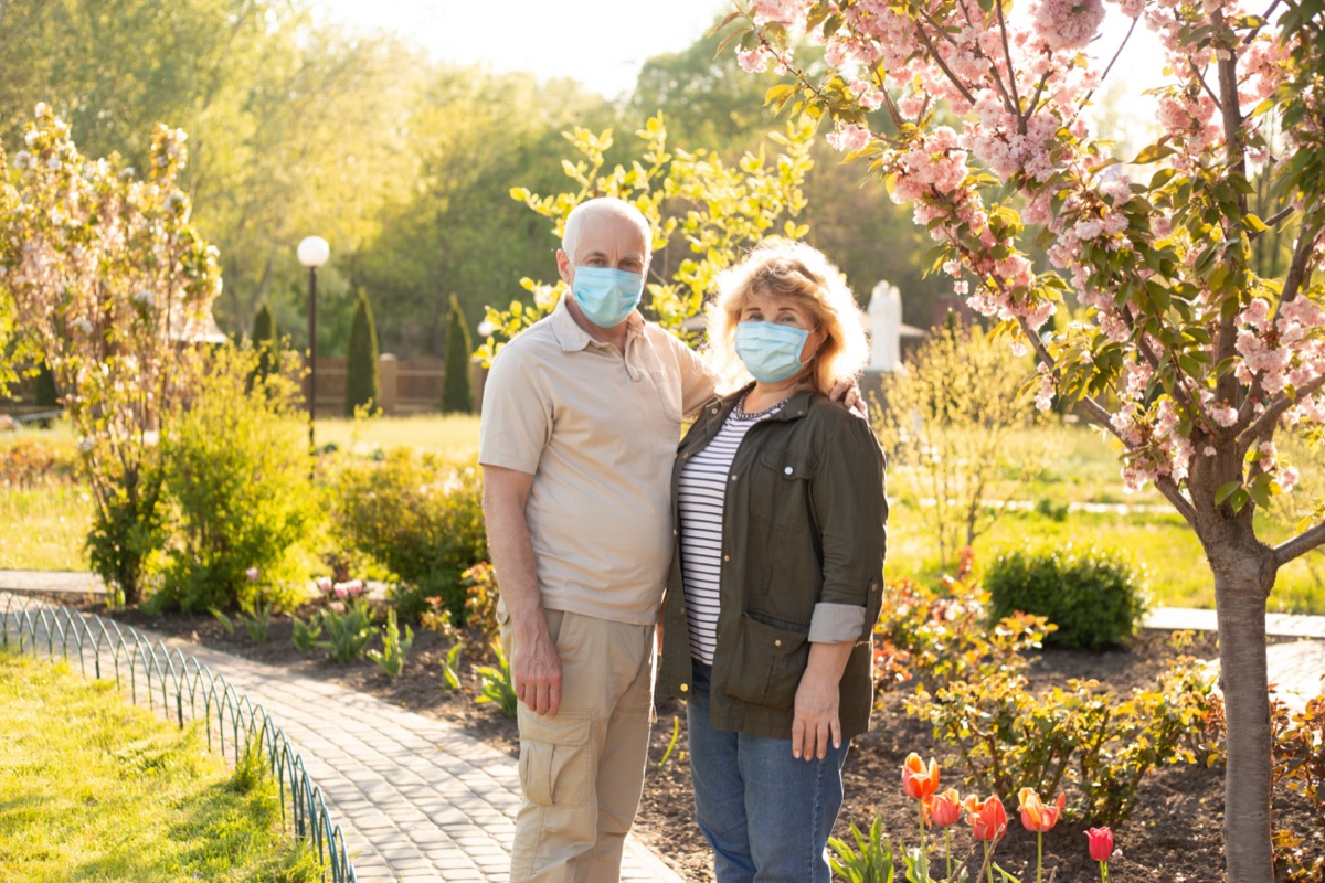 Elderly couple embracing in spring or summer park wearing medical mask to protect from coronavirus
