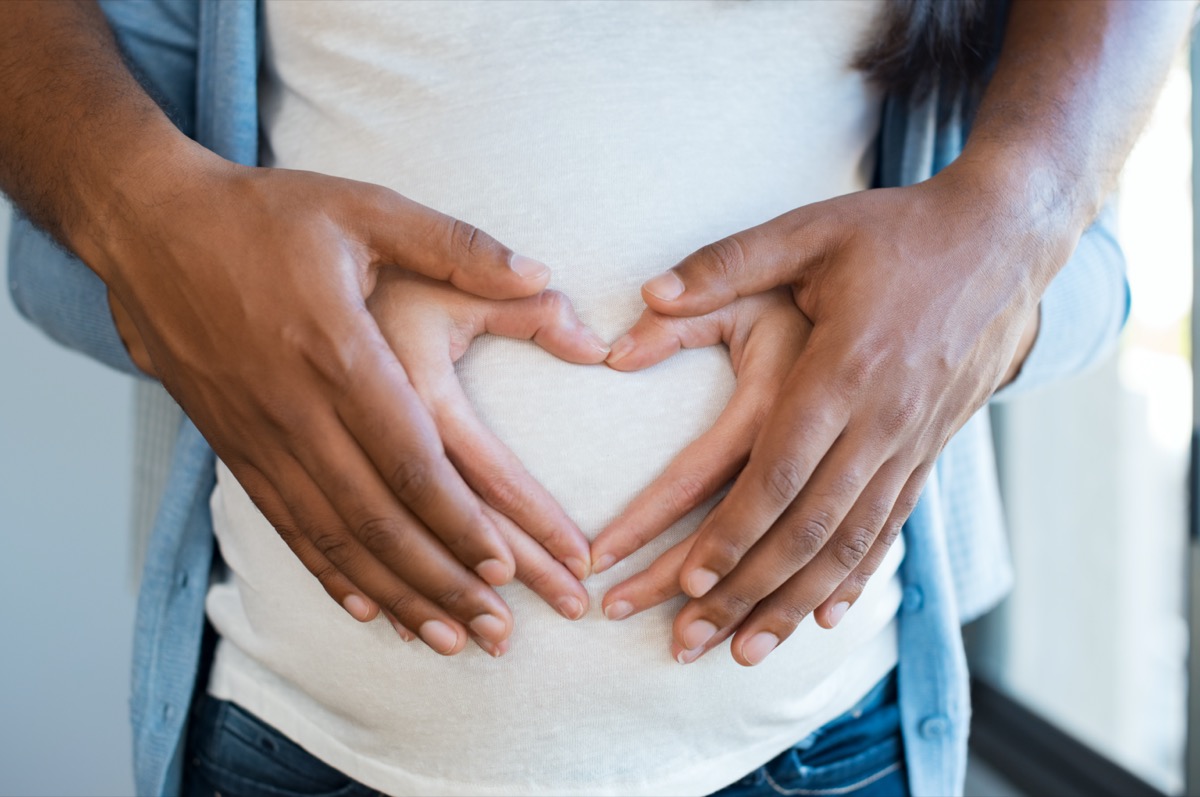 Black man holding belly of his pregnant wife making heart