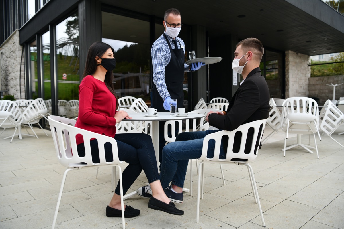 Waiter with protective medical mask and gloves serving guest with coffee at an outdoor bar café or restaurant new normal concept reopening after quarantine