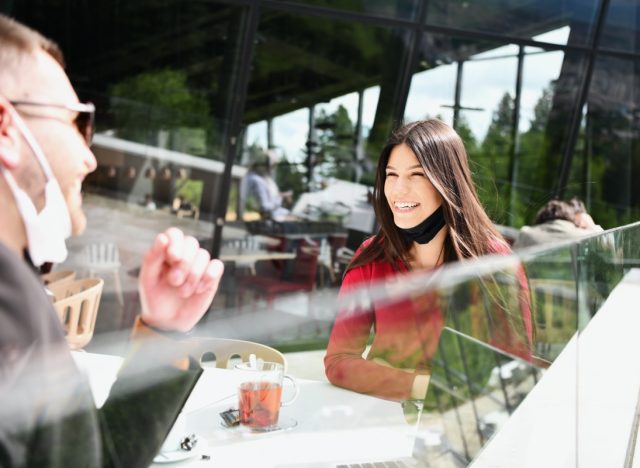 couple with protective medical mask having coffee break in a restaurant, new normal coronavirus concept