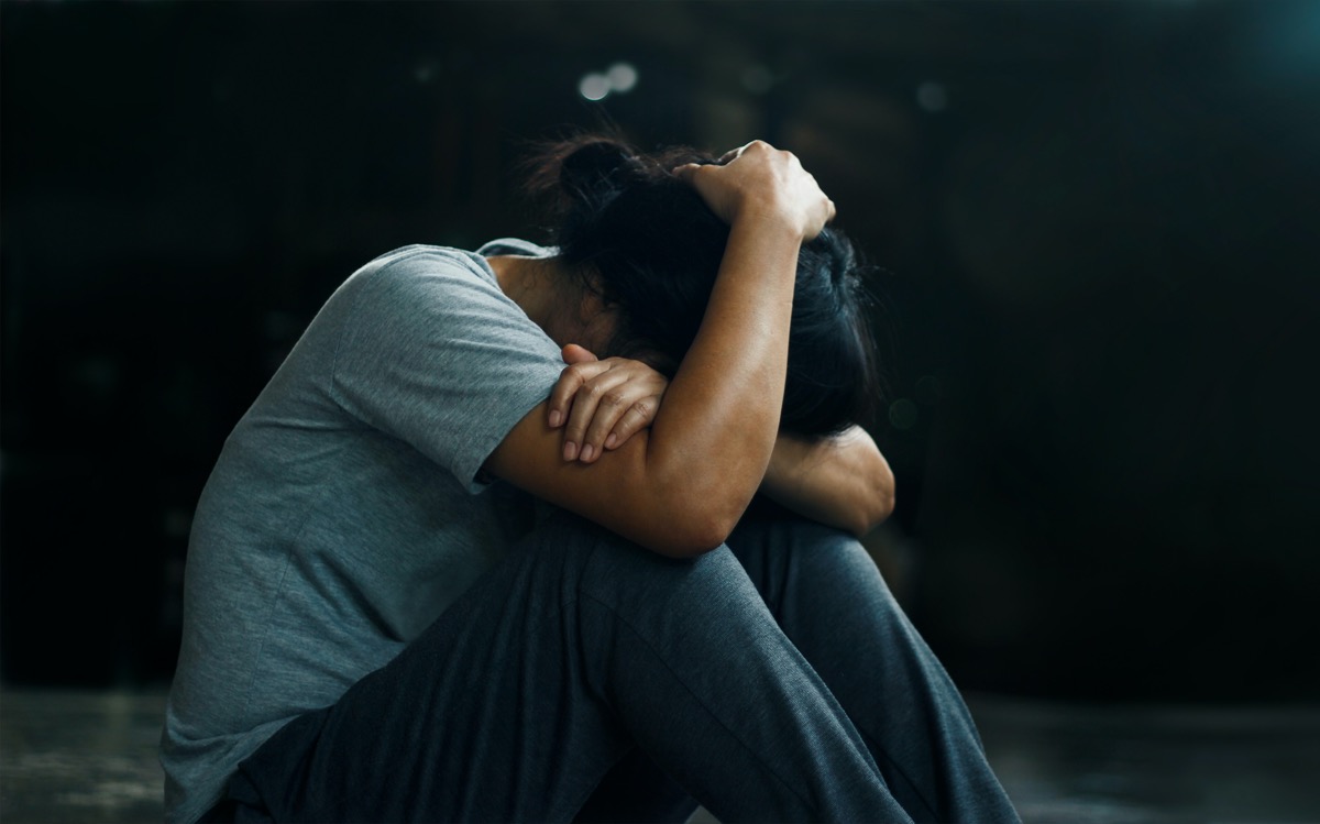 The depressed woman sitting alone on the floor in the dark room background