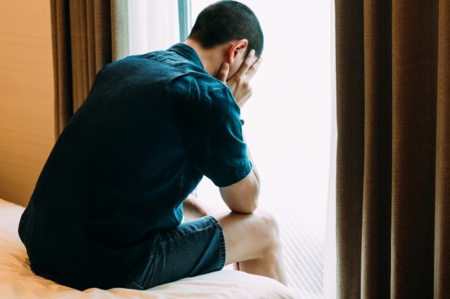 A depressed man with problems sits alone with his hands on the bed and cries
