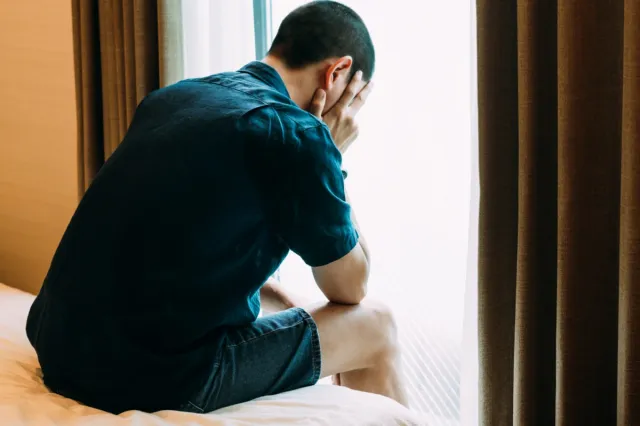 Depressed man with problems sitting alone with his head in his hands in bed and crying