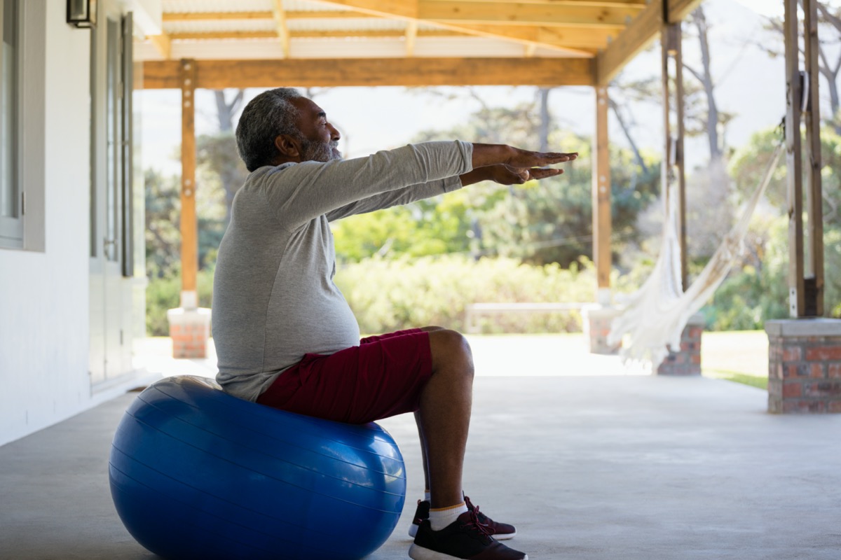 Active senior man exercising on exercise ball in the porch