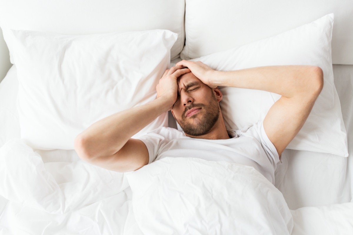 man lying in bed at home suffering from headache