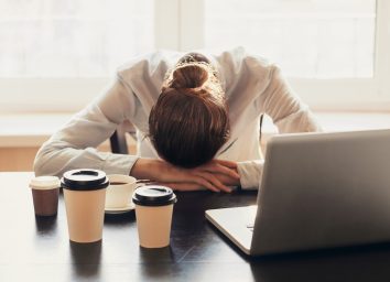 Tired woman working at her desk drinking too much coffee