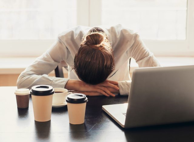 Mujer cansada trabajando en su escritorio bebiendo demasiado café