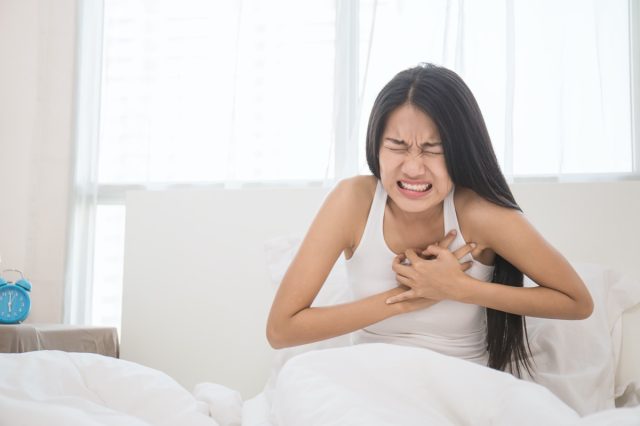 Young woman in pajamas having heart attack in her bedroom (woman, pain, stroke, chest)