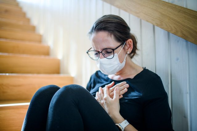 Woman with face mask and chest pain sitting indoors at home