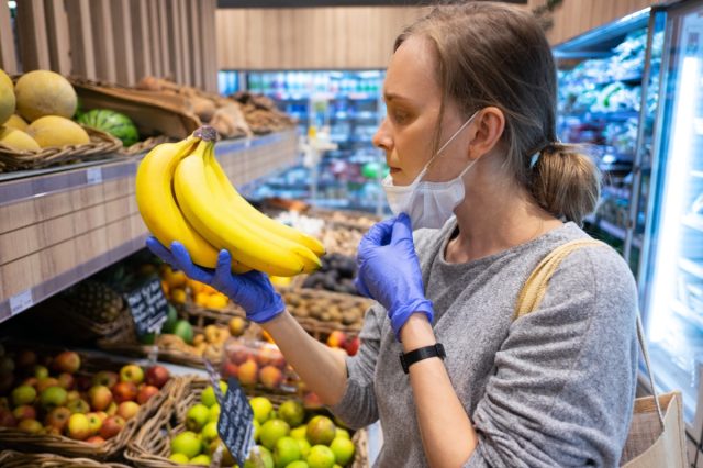 Focused woman taking off face mask while choosing fruits in grocery store.