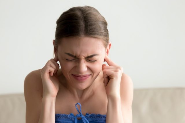 woman sticking fingers in ears with eyes closed, not listening to loud noise