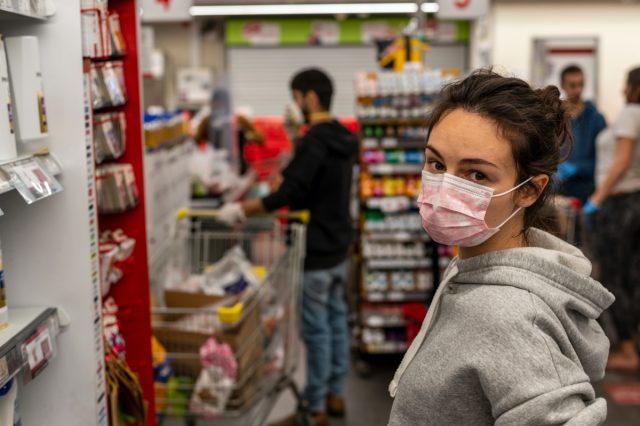 girl in a protective medical mask looks at the camera and stands in line at the cash register in a supermarket
