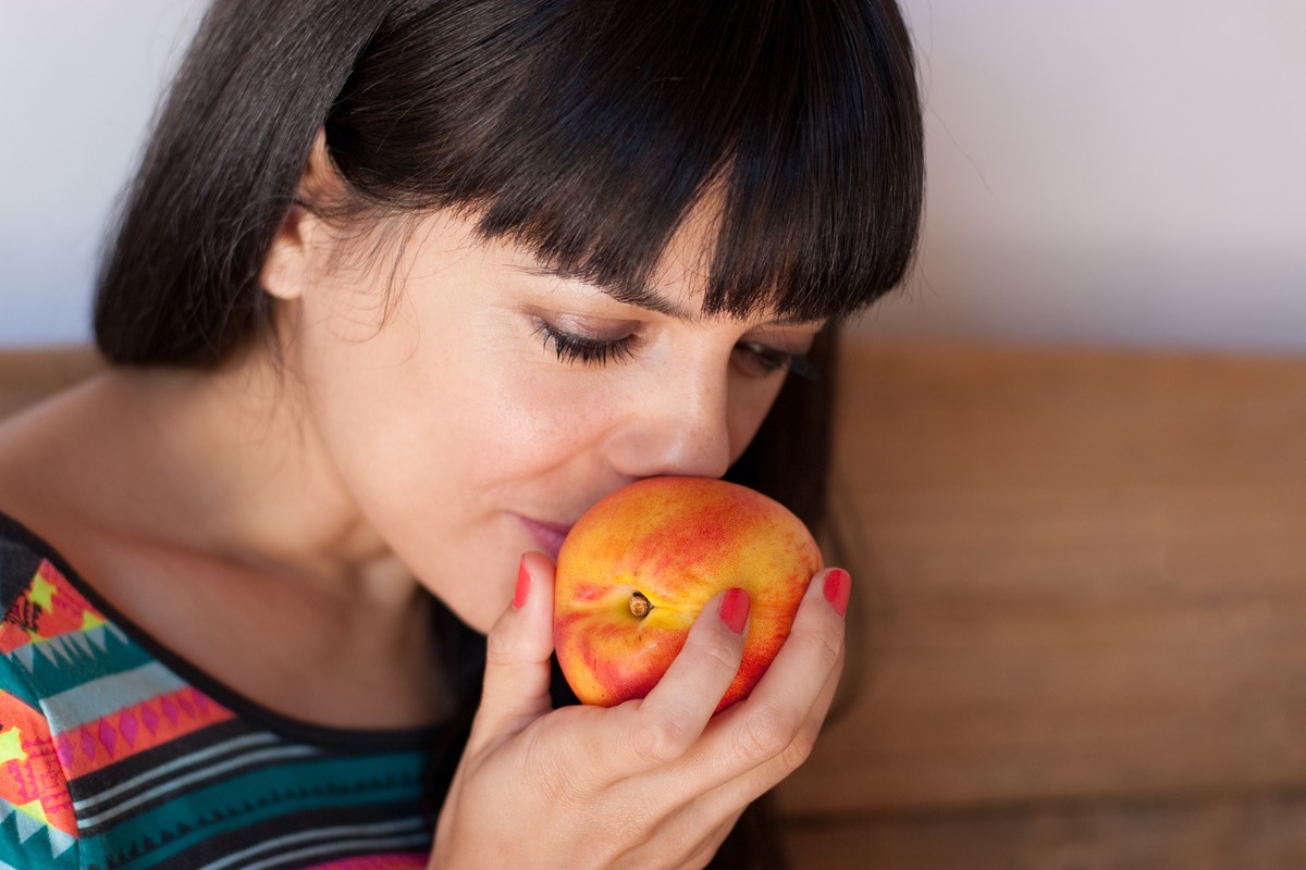 Portrait of young woman smelling a fresh and sweet nectarine