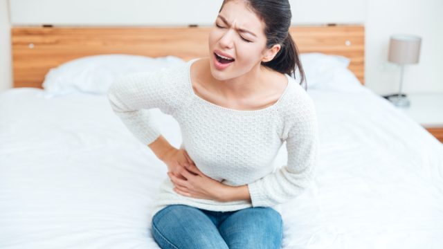 Woman sitting on the bed and touching her left side in pain at home