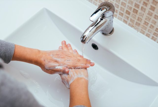 A woman washes her hands with soap and water in the home bathroom