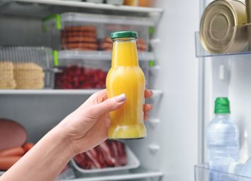 Unhealthy orange juice bottle held in front of fridge