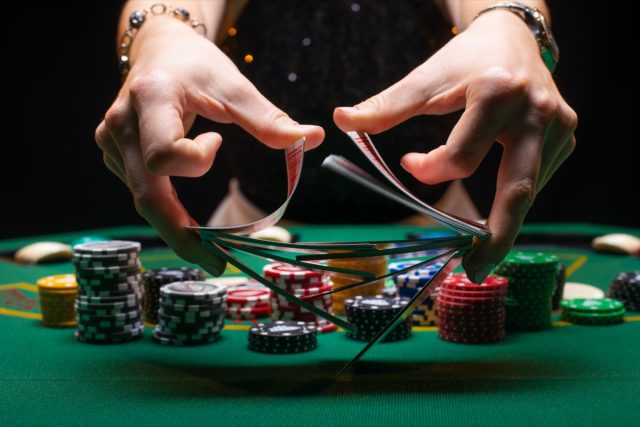 Woman dealer or croupier shuffles poker cards in a casino on the background of a table, chips