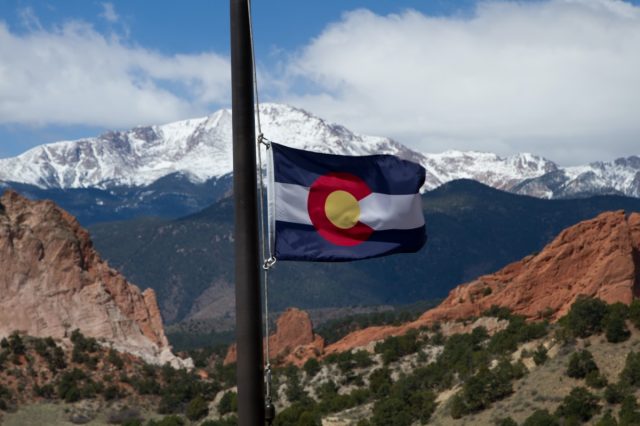 Colorado State Flag with Pikes Peak and Garden of the Gods in the background on a spring day