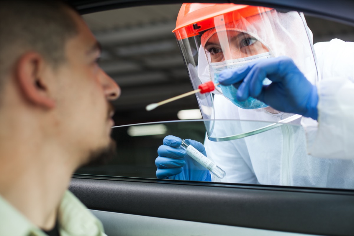 Medical worker performing drive-thru COVID-19 test,taking nasal swab specimen sample from male patient through car window.