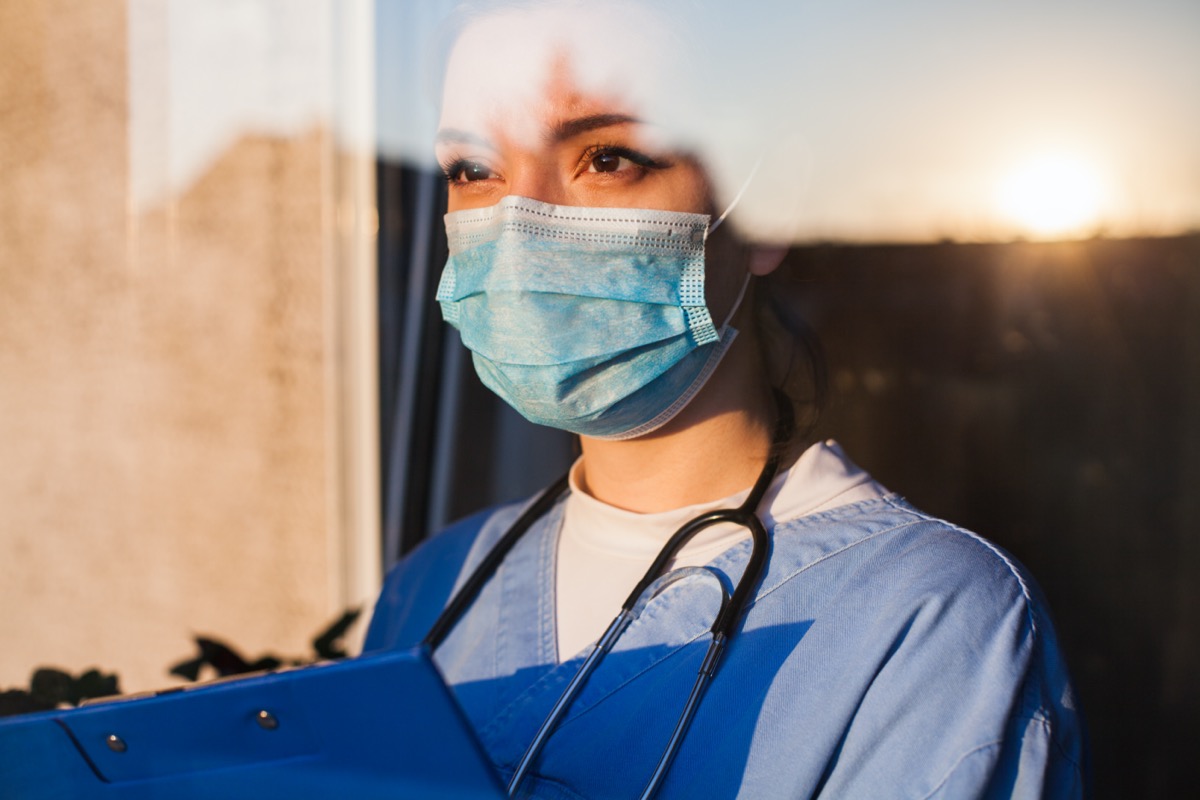 doctor carer looking through ICU window,fear uncertainty in eyes,wearing face mask gazing at sun