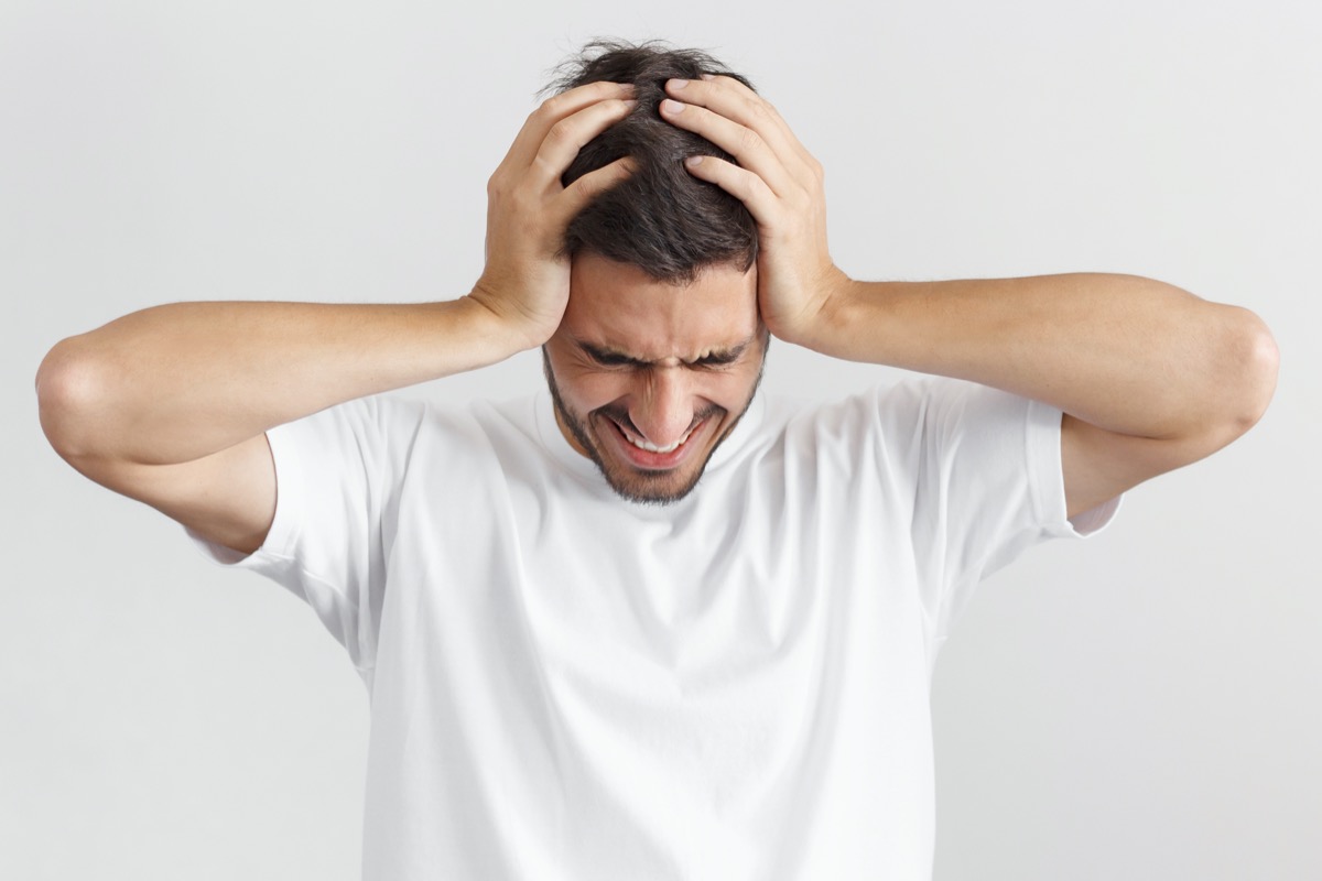 man in white casual t-shirt, holding head with both hands, suffering from severe headache