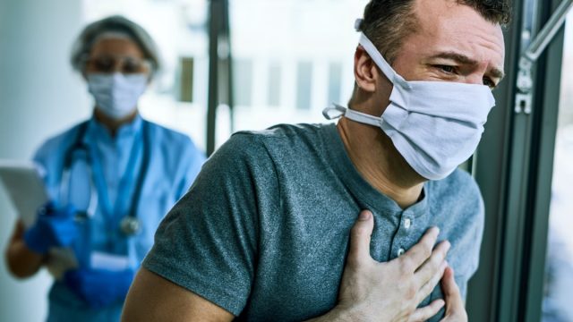 Male patient wearing face mask and feeling chest pain while being at the hospital during coronavirus epidemic