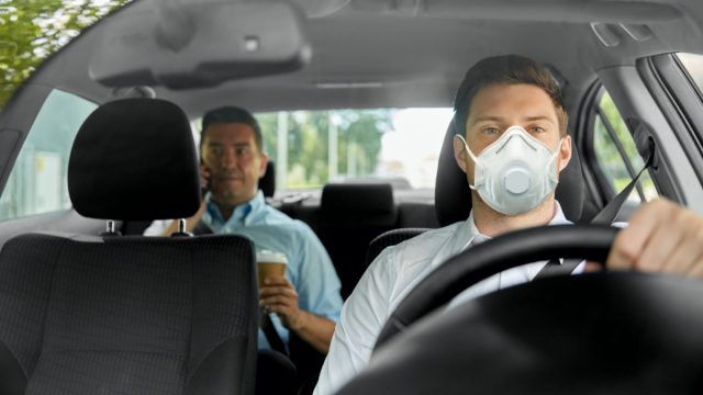 male taxi driver driving car and passenger wearing face protective mask for protection