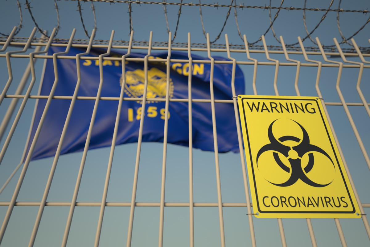 Biohazard coronavirus sign on the barbed wire fence near flag of Oregon.