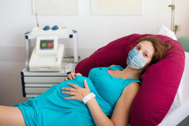 Бременна пациентка, носеща маска за лице в болница по време на лекарско посещение по време на епидемия от коронавирус