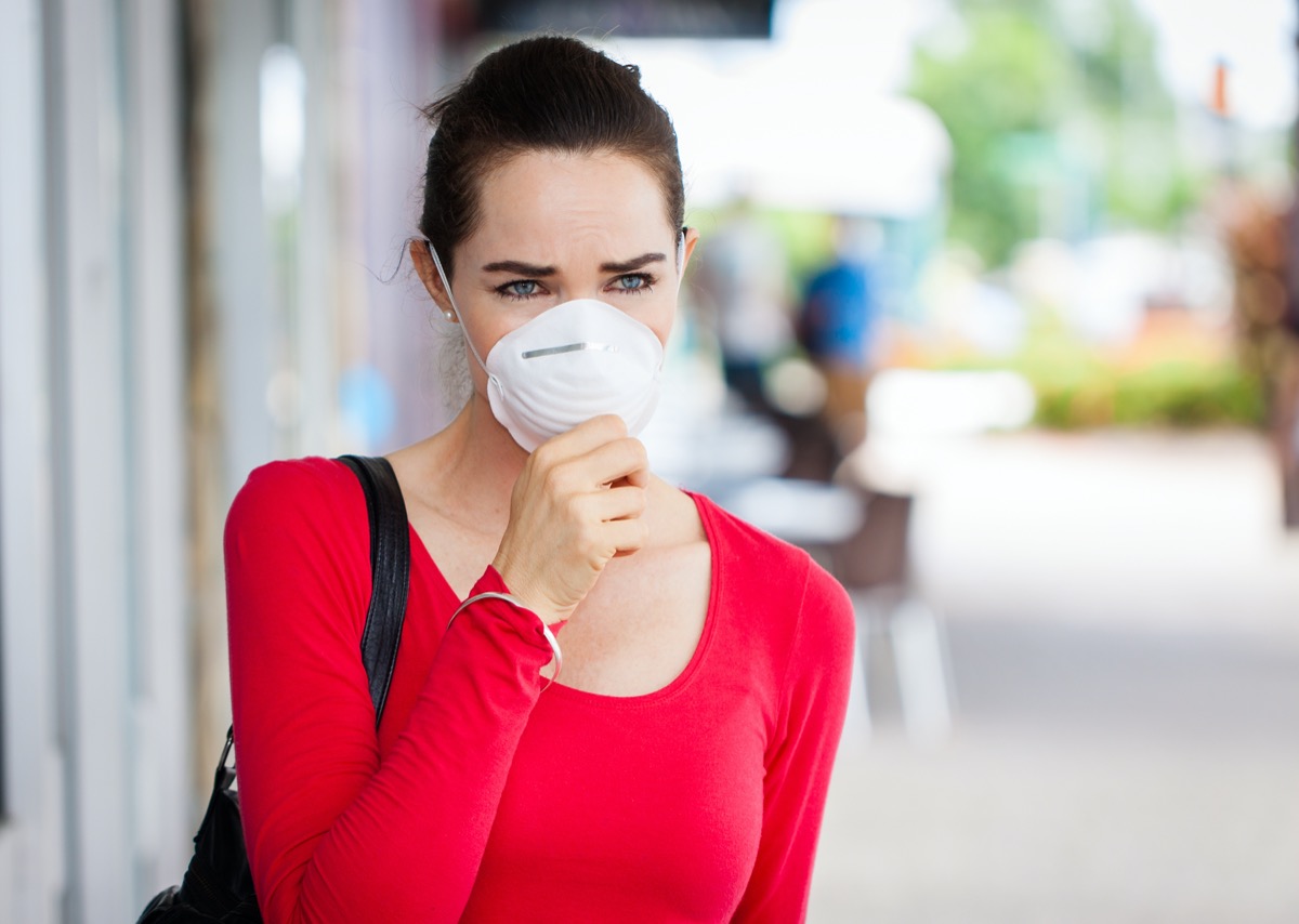 A woman wearing a face mask in the city coughing.