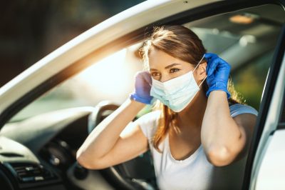woman is putting a mask on her face, to avoid infection during flu virus outbreak and coronavirus epidemic, getting ready to go to work by car