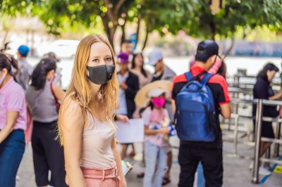 young woman wearing a hygiene protective mask over her face while walking at the crowded place