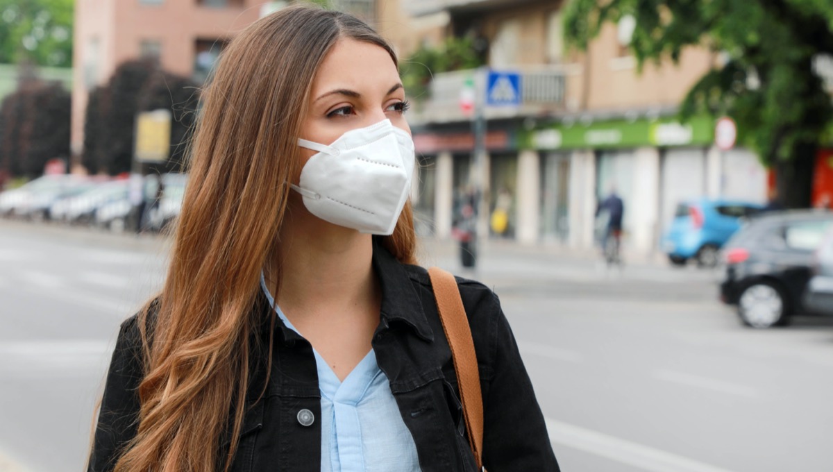 Woman in city street wearing KN95 FFP2 mask protective for spreading of disease virus SARS-CoV-2.