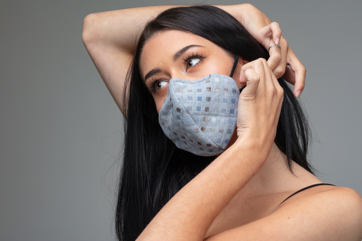 woman adjusting a trendy textile face mask behind her ear.
