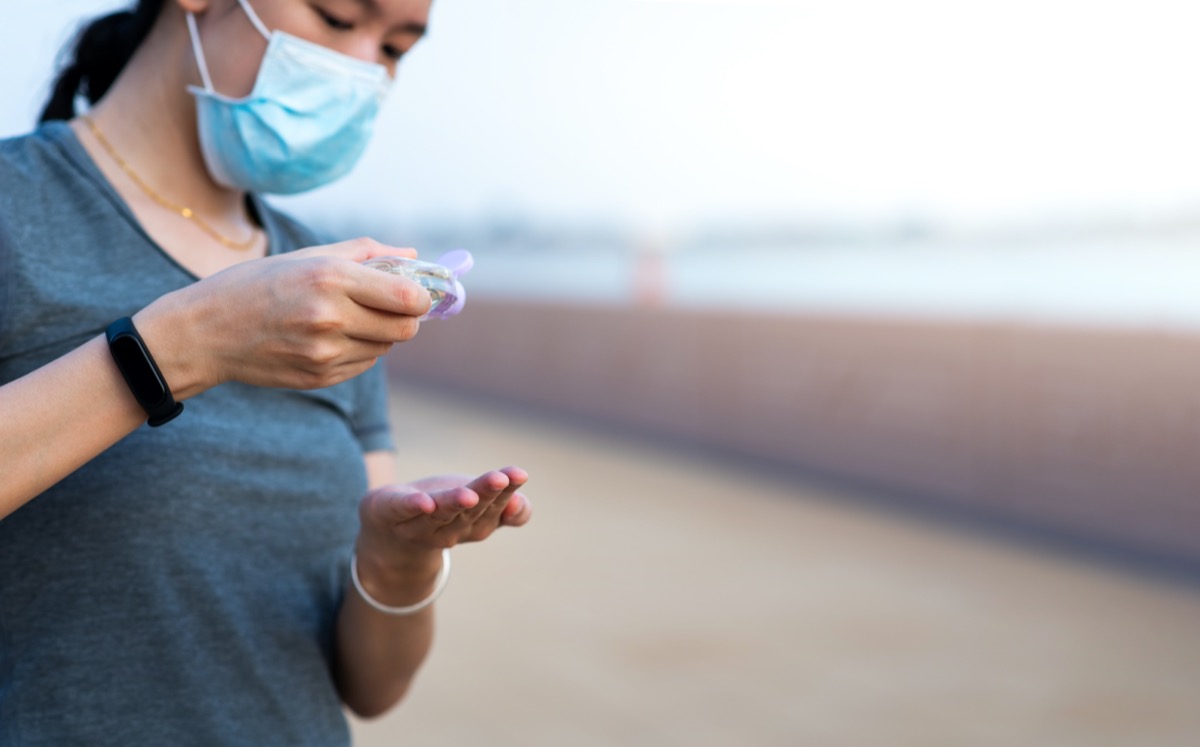 woman using hand sanitizer on the street and wearing face mask as a covid 19 precaution outdoors