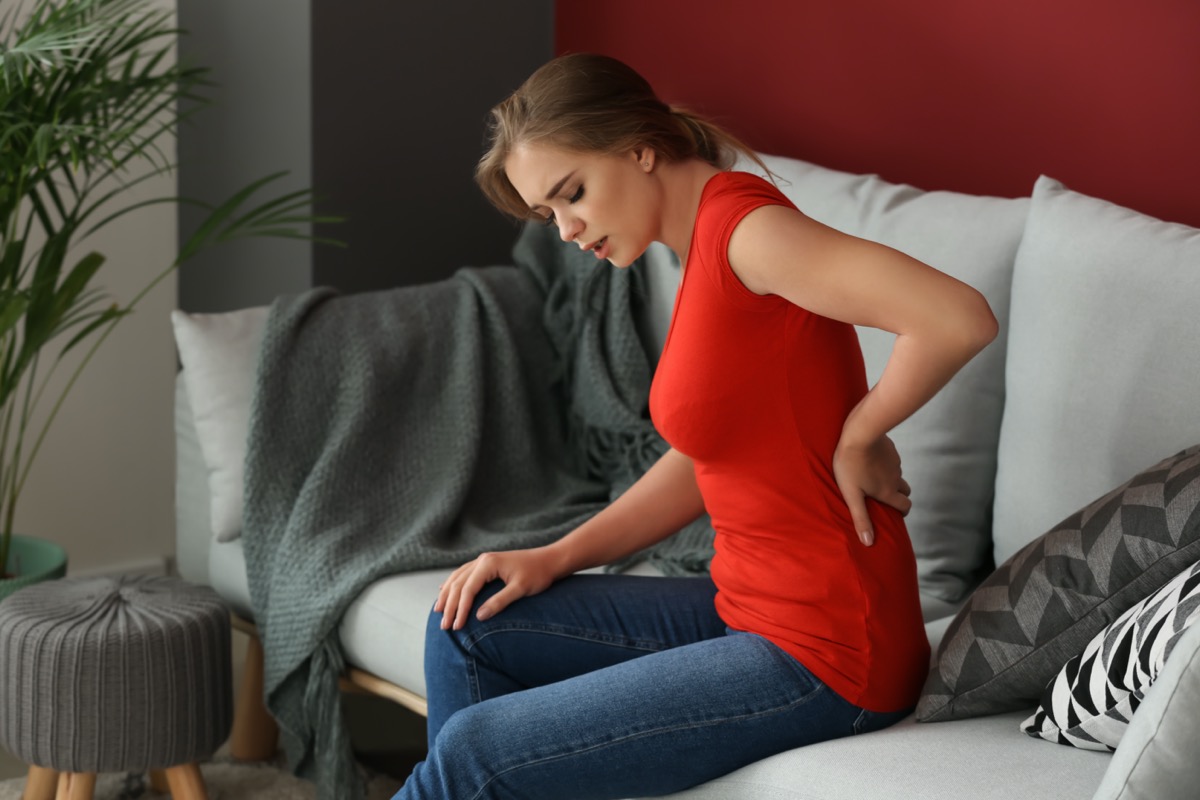 Young woman suffering from back pain while sitting on sofa at home