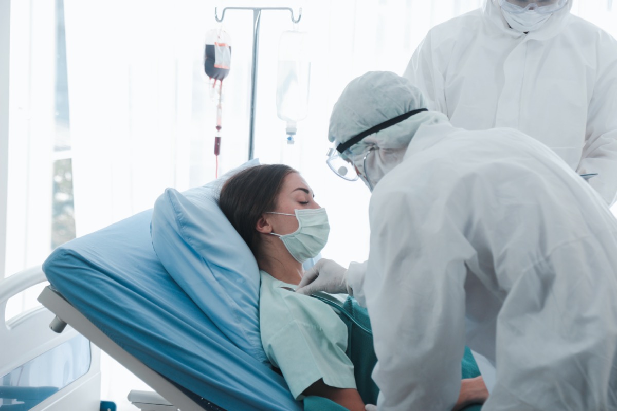 Infected patient woman with face mask lying in bed at disease treatment room, doctor wearing protective clothing take care of the sick in quarantine at hospital