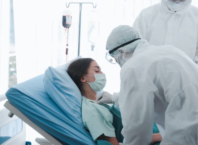 Infected patient woman with face mask lying in bed at disease treatment room, doctor wearing protective clothing take care of the sick in quarantine at hospital