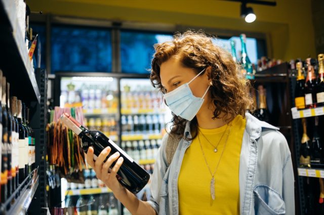 woman wearing protective face mask chooses wine in grocery store