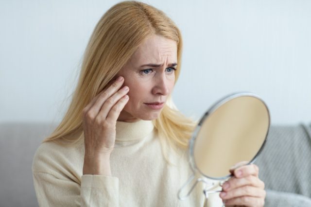 A sad woman matures looking at her wrinkles in the mirror