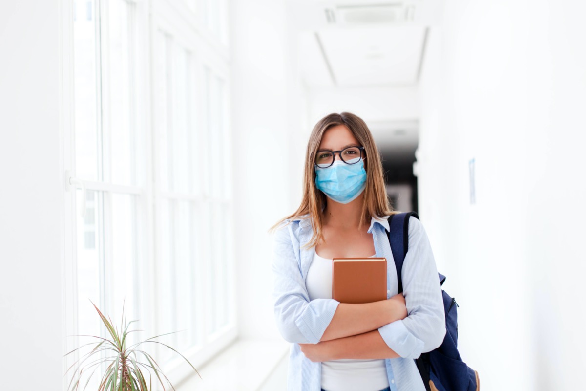 Student in protective face mask in empty college indoors