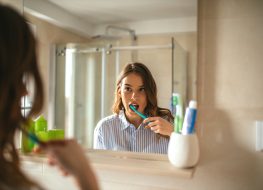 Portrait of a beautiful woman brushing teeth and looking in the mirror in the bathroom.