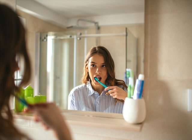Portrait of a beautiful woman brushing teeth and looking in the mirror in the bathroom.