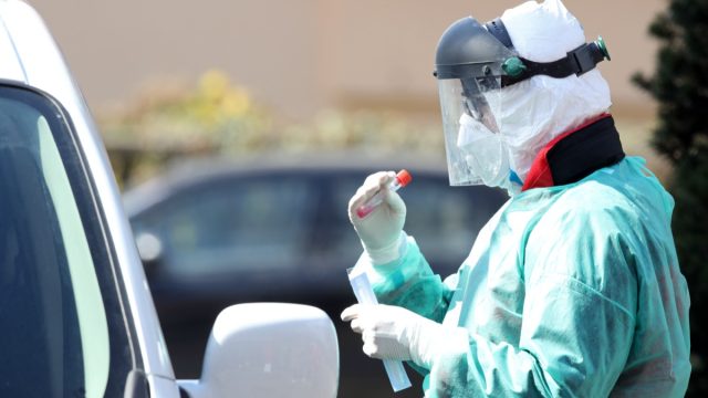 Medical staff member with mask and protective equipment performs Coronavirus nasal swabs test tubes at drive-through testing point in an effort to curb the spread of COVID-19 (novel coronavirus).