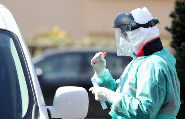 Medical staff member with mask and protective equipment performs Coronavirus nasal swabs test tubes at drive-through testing point in an effort to curb the spread of COVID-19 (novel coronavirus).