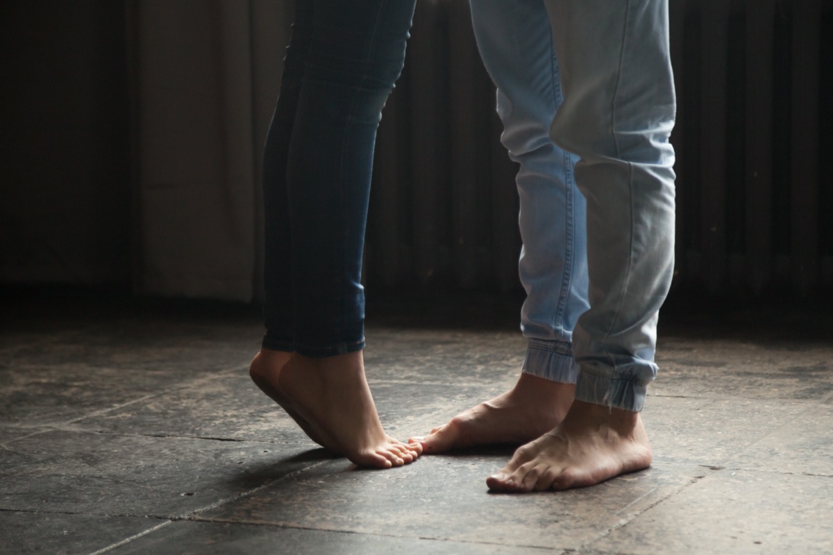 Barefoot girl standing on tiptoes to kiss her man at home