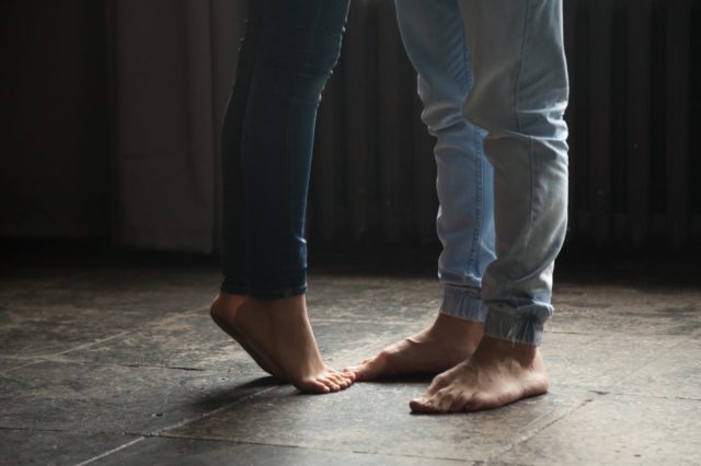 Barefoot girl standing on tiptoe to hug her man at home